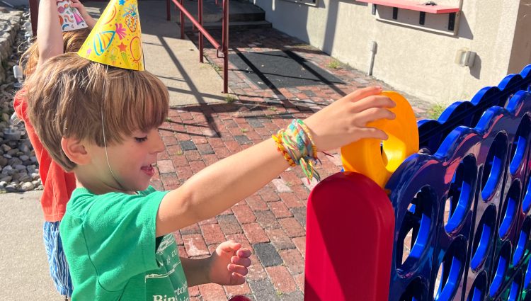 Boy playing with a giant Connect 4 game outside of the Creamery