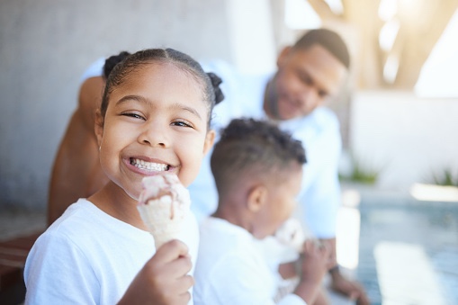 Little girl smiling eating ice cream, with her family in the background